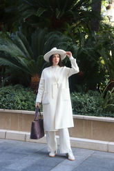 a lady in a white top, a pair of white pants and a long white wool coat